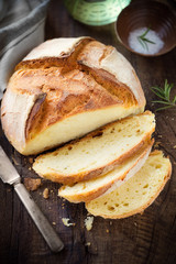 Freshly baked homemade bread on dark rustic wooden table with salt and olive oil at the background