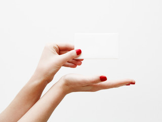 Flat lay, top view. Beauty and fashion concept. Beautiful female hands with red manicure. Minimal style. Minimalist photography. Pale composition with girl's hand holding card on white background