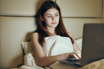 Young beautiful woman working at computer at home in bedroom in bed