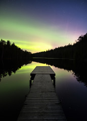 Fototapeta na wymiar Scenic aurora borealis with nice reflections and pier at night in Finland