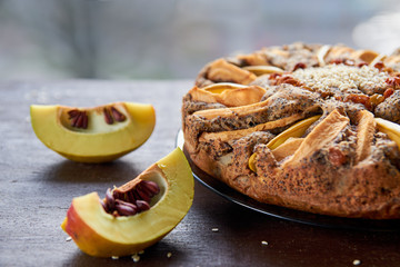 A piece of apple tart with quince, poppy seeds, raisins and sesame on wooden brown table. Apple pie decorated with sliced fresh quince and sesame seeds on the blurred background. Close up view 