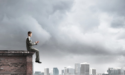 Man on roof edge send message with smartphone and cityscape at background