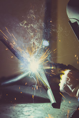 Worker with protective mask welding metal and producing smoke and sparks