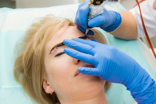 Beautiful woman with smooth, young skin, sitting in a beautician. A beautician performs modeling permanent eyebrows makings.