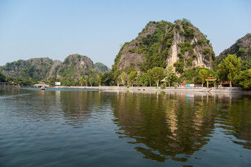 Fototapeta na wymiar Houses and on a background of rocks on the river Ngo Dong. Ninh Binh Province, Ha Long Bay on land, Vietnam