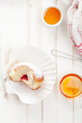 Tea time with festive sufganiyot donuts filled with jelly and covered with sugar powder. White wooden background, bright lighting. Vertical composition.