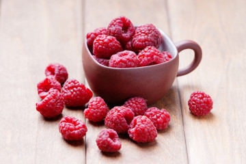 Raspberries in a cup and on a wooden table