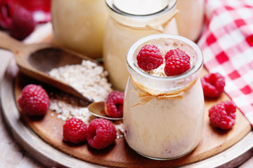 Jars with yogurt, raspberries, wooden scoop and oat flakes 