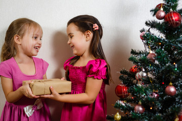 Fototapeta na wymiar two happy little sisters at home with Christmas tree and presents. On a white background.