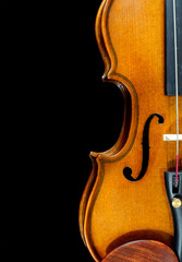 Closeup detail of miniature violin on black background includes a sound hole, chin rest and features the beautiful curves of the wooden instrument