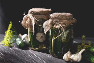 Two jars of pickled cucumbers with garlic and dill on black table