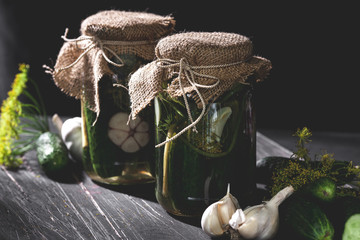 Rustic jars of  pickled cucumbers with garlic and dill on black table