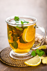 Hot herbal tea with fresh lemon, ginger and mint leaves on brown background, closeup