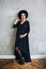 Caucasian pregnant woman with make up in black dress and black hat, portrait of future mother, happy pregnancy, fasion portrait