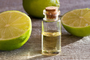 A bottle of lime essential oil with fresh limes