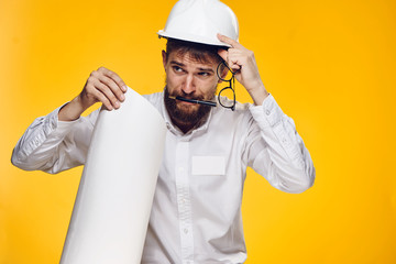 Male engineer straightens construction helmet and keeps glasses on yellow background