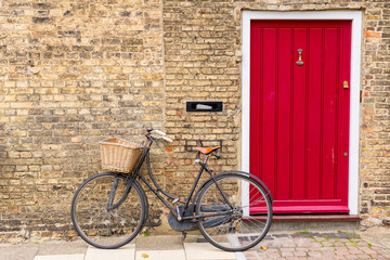 Fototapeta na wymiar Vintage bicycle with retro wicker basket parked in front of a house brick wall next to a bright red door
