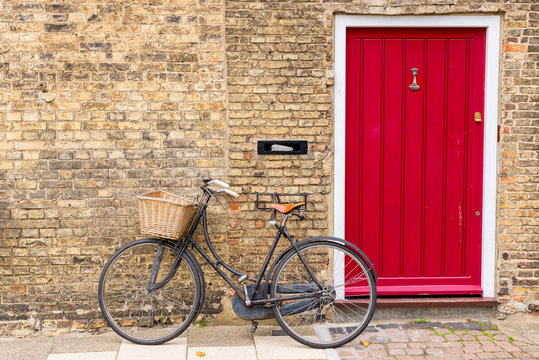 Vintage bicycle with retro wicker basket parked in front of a house brick wall next to a bright red door