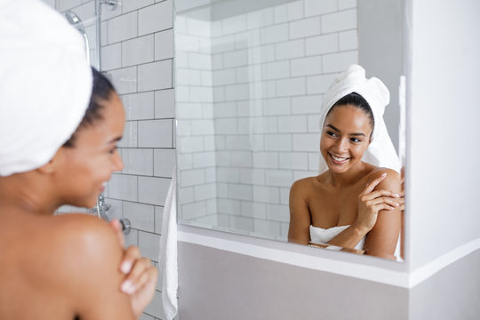 Beautiful mixed race woman looking at her reflection in mirror, touching a shoulder