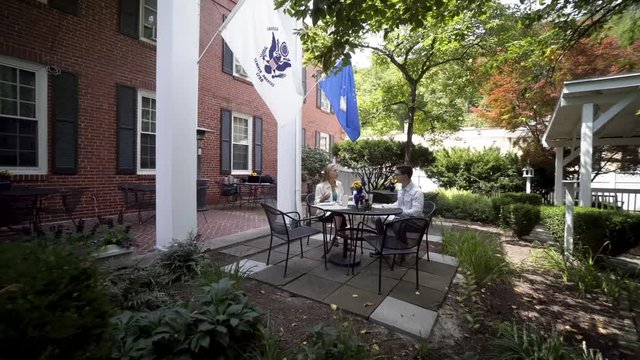 Camera orbits around a mature mother and hipster teen son sit at an outdoor table and wait for their meal to be delivered.
