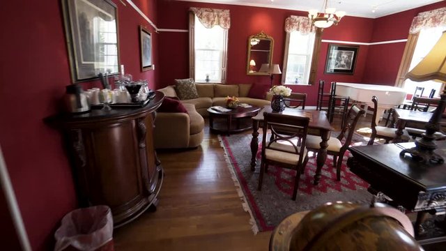 Steadicam walk through a beautiful red lounge sitting room with a fireplace, tables, flowers lamps and a white grand piano in a historic inn.