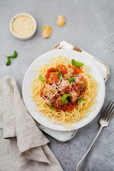 Pasta spaghetti with tomato sauce, parmesan cheese, basil and meatballs on white ceramic plate on gray concrete or stone background. Selective focus. Top view.