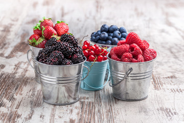 Colorful berries assortment in five tin cans on rustic wooden table blueberry, raspberry, red currant, strawberry, in five old tin cans on rustic wooden table in studio