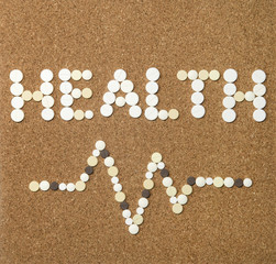 Fototapeta na wymiar The word health written with pills and a cardiogram lane on a cork background. Health issue concept.