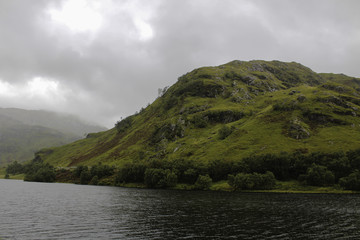 A Cloudy sky rolls over a lush green lakeside on Lock Lomond in the western highlands of Scotland