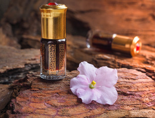 Bottle of oil agarwood tree against the bark. Arabian oud attar perfume or agarwood oil fragrances in mini bottle.
