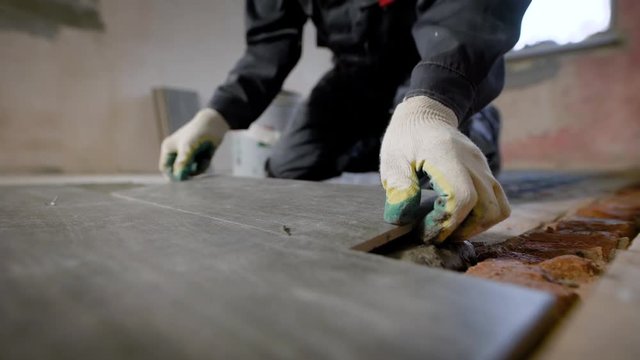 Close look at the constuction worker laying down the tile on cemented floor.