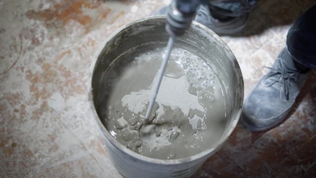Close up shot of a builder mixing cement in a bucket on a constraction site with a special tools.