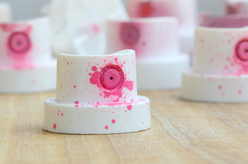 Several plastic nozzles from a paint sprayer that lie on a wooden surface against a gray wall background. The caps are smeared in pink paint. The concept of street art and graffiti © mehaniq41