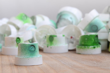 Several plastic nozzles from a paint sprayer that lie on a wooden surface against a gray wall background. The caps are smeared in green paint. The concept of street art and graffiti © mehaniq41
