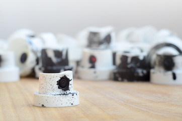 Several plastic nozzles from a paint sprayer that lie on a wooden surface against a gray wall background. The caps are smeared in black paint. The concept of street art and graffiti © mehaniq41