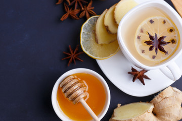 Hot spicy ginger tea in white cup with lemon, honey and spices on black background, flat lay with copy space