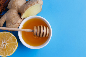 Ingredients for spicy warming ginger tea. Ginger root, honey, lemon and spices on blue background with copy space, view from above