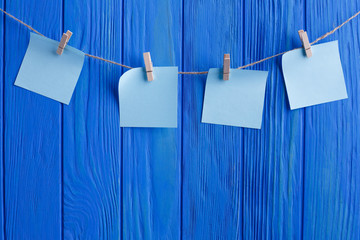 Creative reminder, small sheets of paper on old clothespin. Sales, notices concept. Four blue blank stickers on the rope on blue wooden plank background with copy space for your text design.