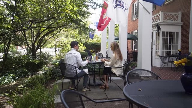 Camera starts at an empty table and moves in to a mature mother and hipster teen son sitting at an outdoor table waiting for their lunch or dinner to be delivered.