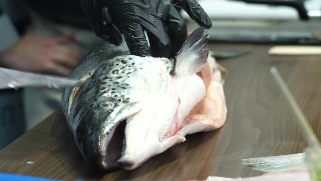Men's hands in black gloves cut off the head of a fish