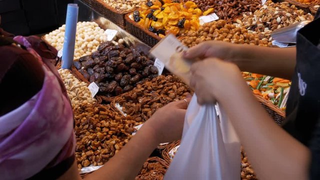 The buyer gives money to the seller for purchased dried fruits in La Boqueria. Barcelona. Spain. Nuts, dry fruits on display at the market on the showcase. Stall with Various dried fruits at Mercat de