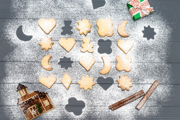 Christmas different shaped cookies with sugar powder and chiristmas ornaments, sticks of cinnamon on wooden table