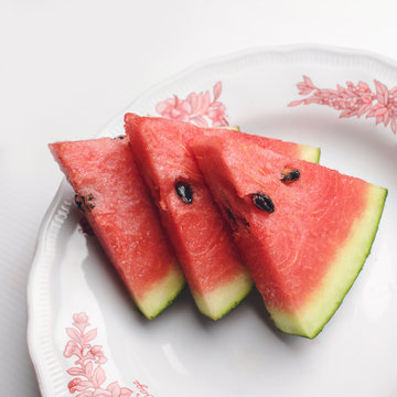 Watermelon is a piece Placed on a white saucer.