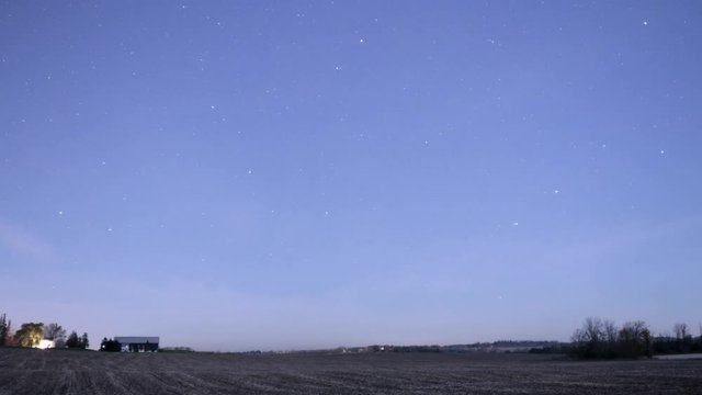 Stars moving over farm fields and farm house in rural area in night sky in light polluted suburb of Toronto. The direction is north.