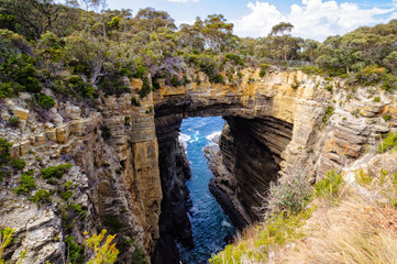 The huge solid rock bridge of the Tasman Arch  spans the gap across the chasm created by the wind and waves over millions of years - Eaglehawk Neck, Tasmania, Australia