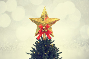 Gold glitter star decoration on top of a Christmas tree with blur background