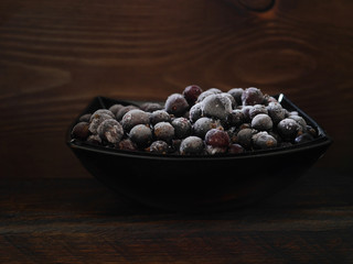 Frozen black currant in a black cup on a dark wooden background. Dark light.