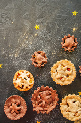 Different sizes of traditional Christmas dessert - Mince pies. Vanilla and chocolate pastry. Black backdrop.Top view.