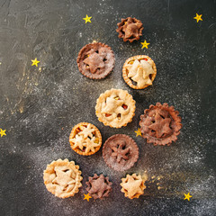 Different sizes of traditional Christmas dessert - Mince pies. Vanilla and chocolate pastry. Black backdrop.Top view.