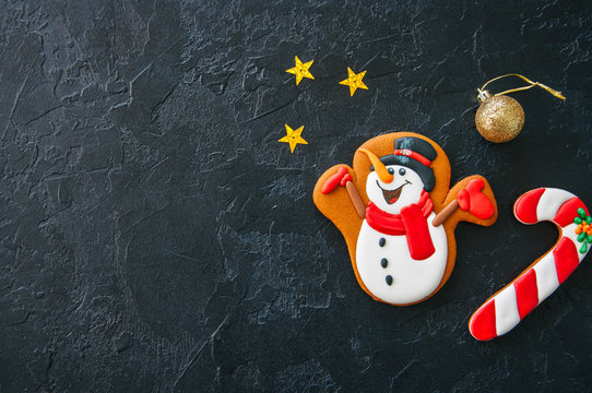 Festive Christmas background, Cookies with image of Snowman, candy cane,  stars and ball on a black stone background. Top view with copy space.
